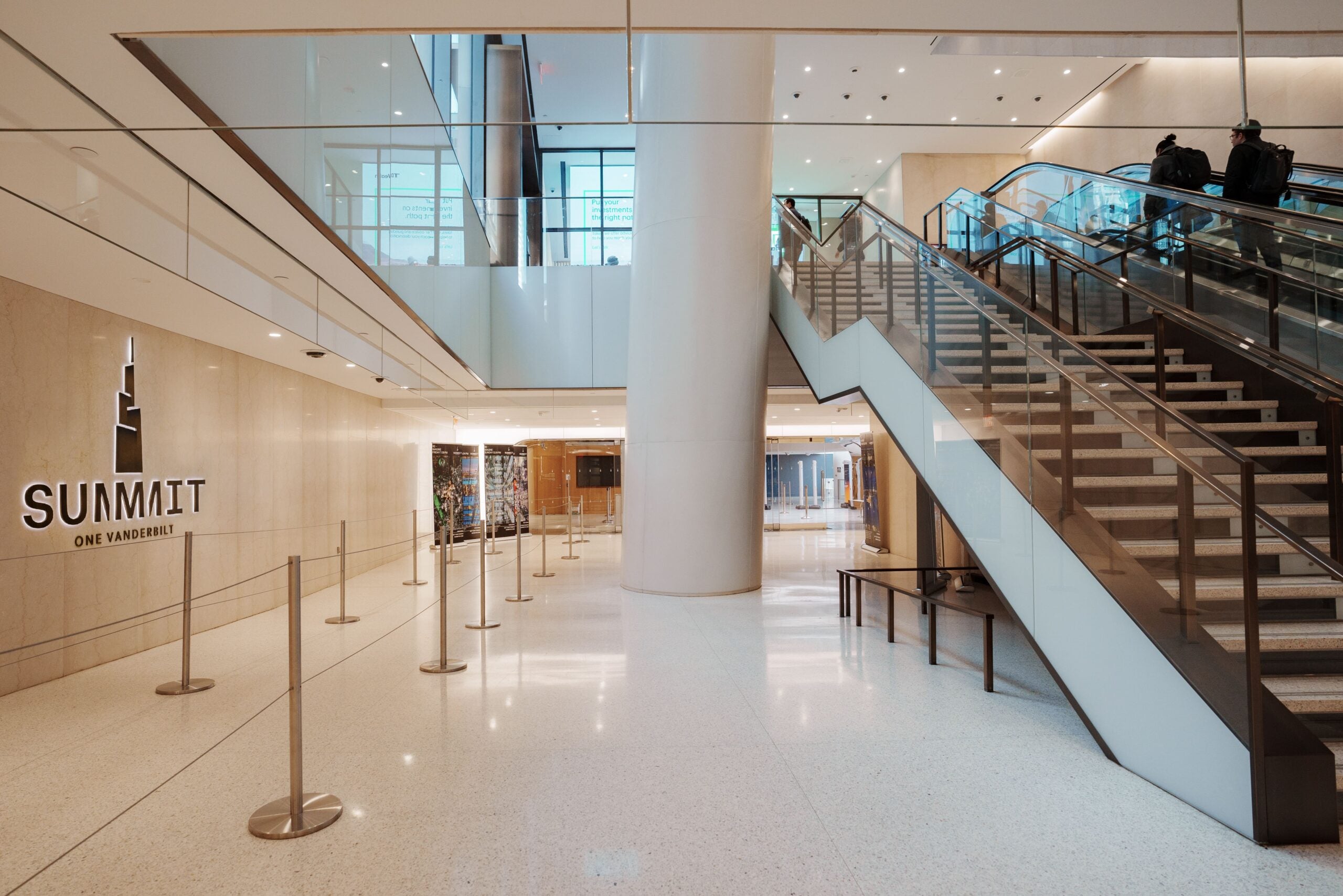 SUMMIT One Vanderbilt’s entrance is located on the Basement level (B1) of One Vanderbilt building, and is accessed from Grand Central Station. The Welcome Center is located right in front of the entrance, and is a warm space with areas for ticket purchasing at kiosks along the walls and a Box Office desk staffed by SUMMIT Guest Ambassadors dressed in navy blue. A large screen is located to the left of the desk, and displays ticketing information for general admission, as well as add-on packages. Guests who arrive with tickets that have been pre-purchased online can move quickly through this space and onto the security scan after they acquire a wristband that can be scanned later to collect photos taken throughout SUMMIT. Photo Ambassadors will put wristbands on guests, or guests can put on their wristbands on their own.