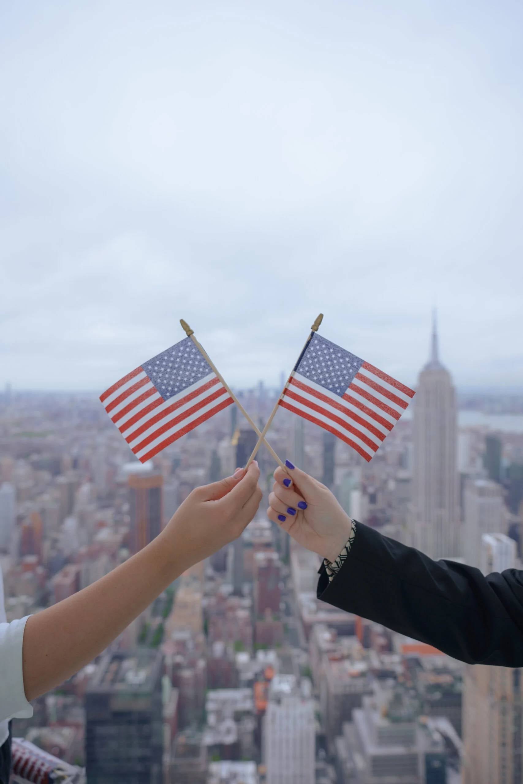 Two people holding American flags with the New York City skyline and Empire State Building in the background.